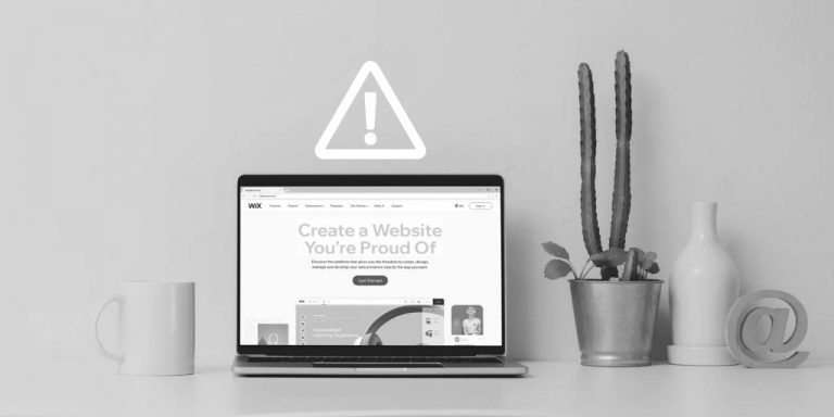 Wix.com (not recommended) pulled up on laptop screen next to mug, cactus, vase, and @ symbol sign