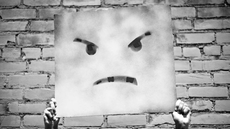 Hands holding up an angry face painted on a square canvas