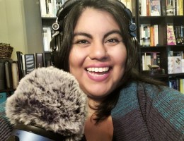 A photo of Jennifer van Alstyne, owner of The Academic Designer. Jennifer is wearing headphones and smiling in front of a microphone with a fuzzy wind cover.