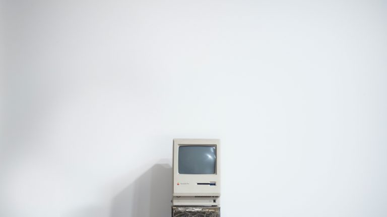 An old Macintosh computer with a floppy disk drive against a white wall