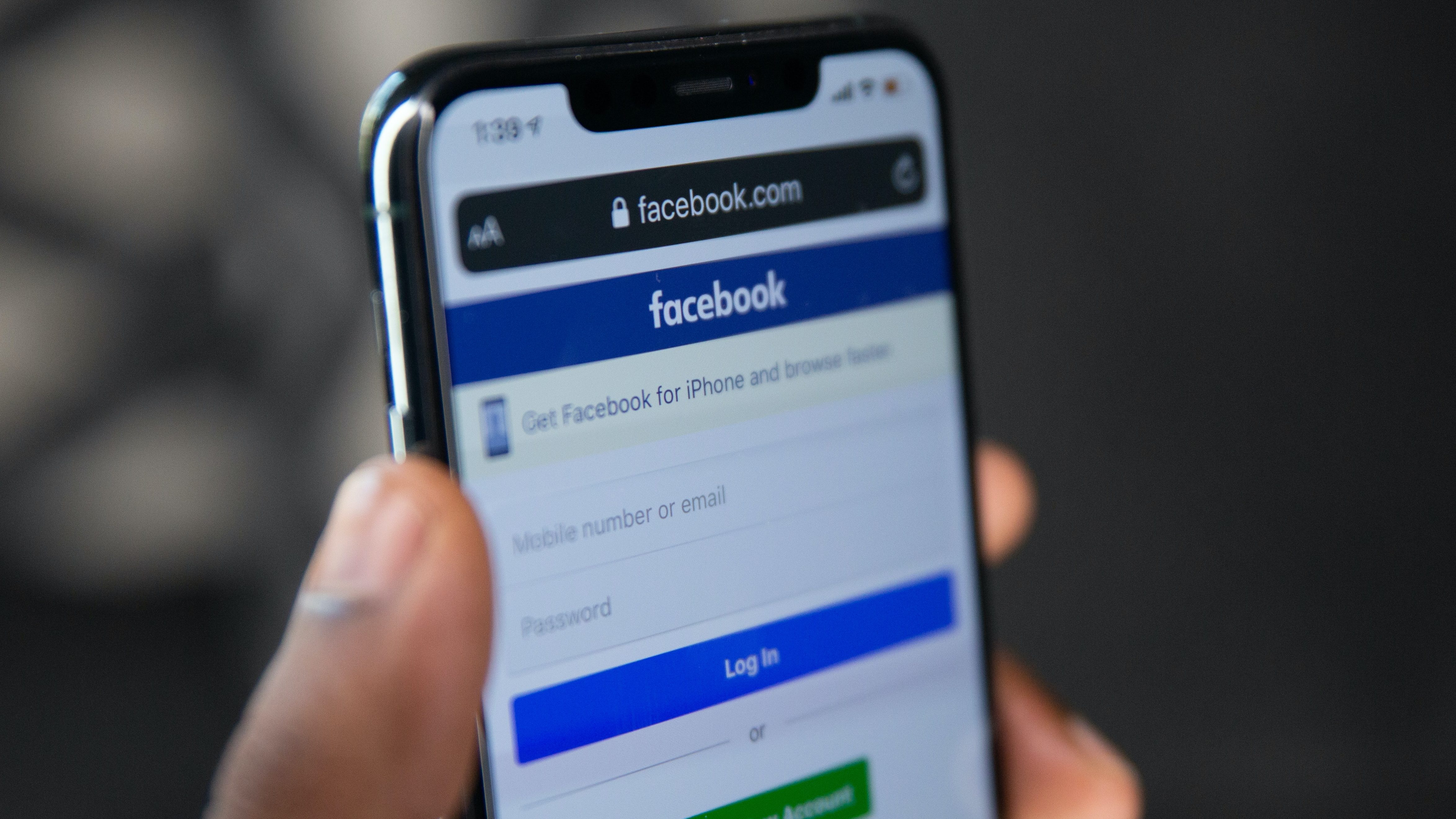 A black person's hand holding a cell phone with the Facebook mobile log-in screen pulled up.