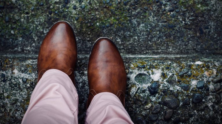 A close up of someone's brown leather shoes and tan slacks as they get ready to step down a stair.