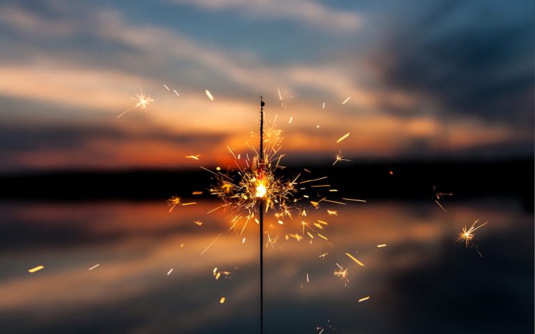 A lit sparkler in front of a blurred background of a sunset.