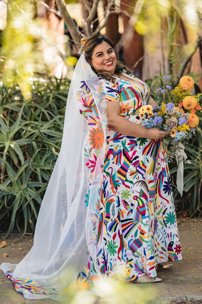 Jennifer poses in her wedding dress and veil, hand embroidered by Otomi women, designed by Martha Aguilar from Arte Otomi. Jennifer holds her bouquet in her hands.