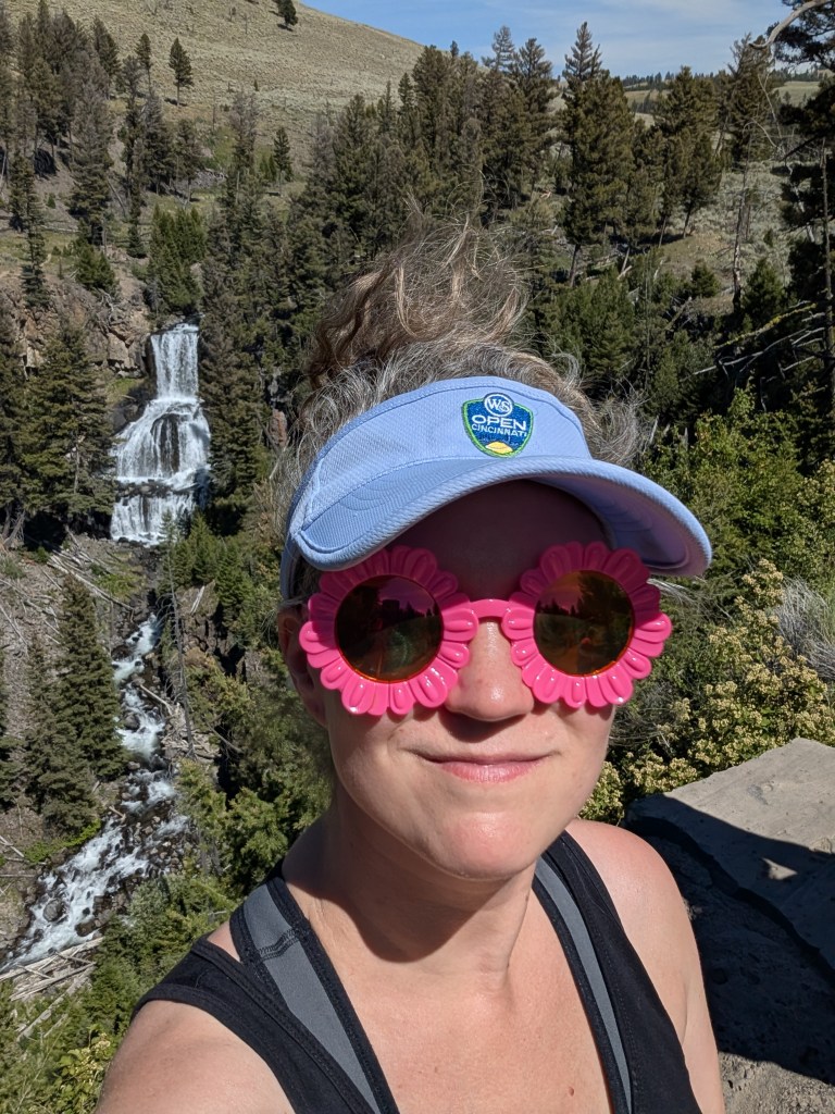 Dr. Katy Peplin is hiking. She's wearing a light blue visor and bright pink sunglasses.